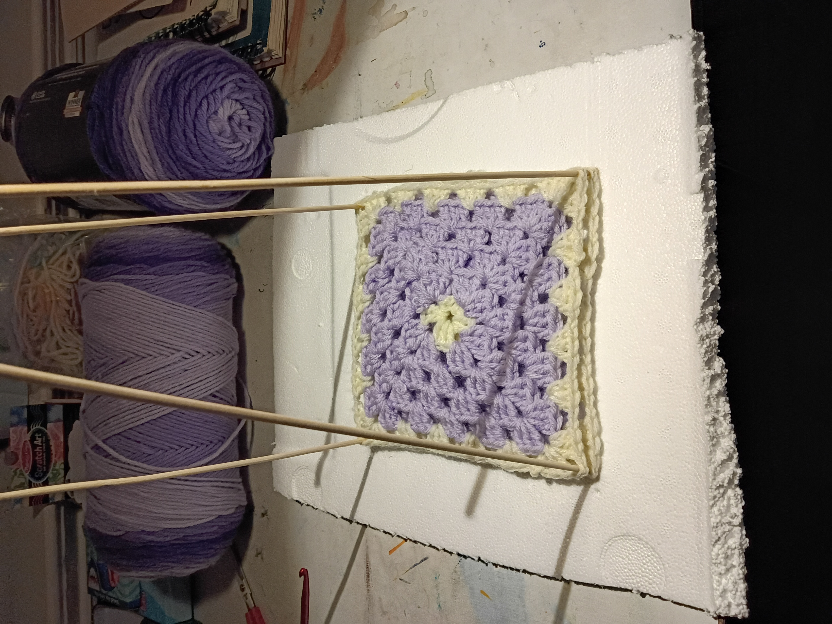 a few purple and white granny squares in a blocking pad made from foam and skewers