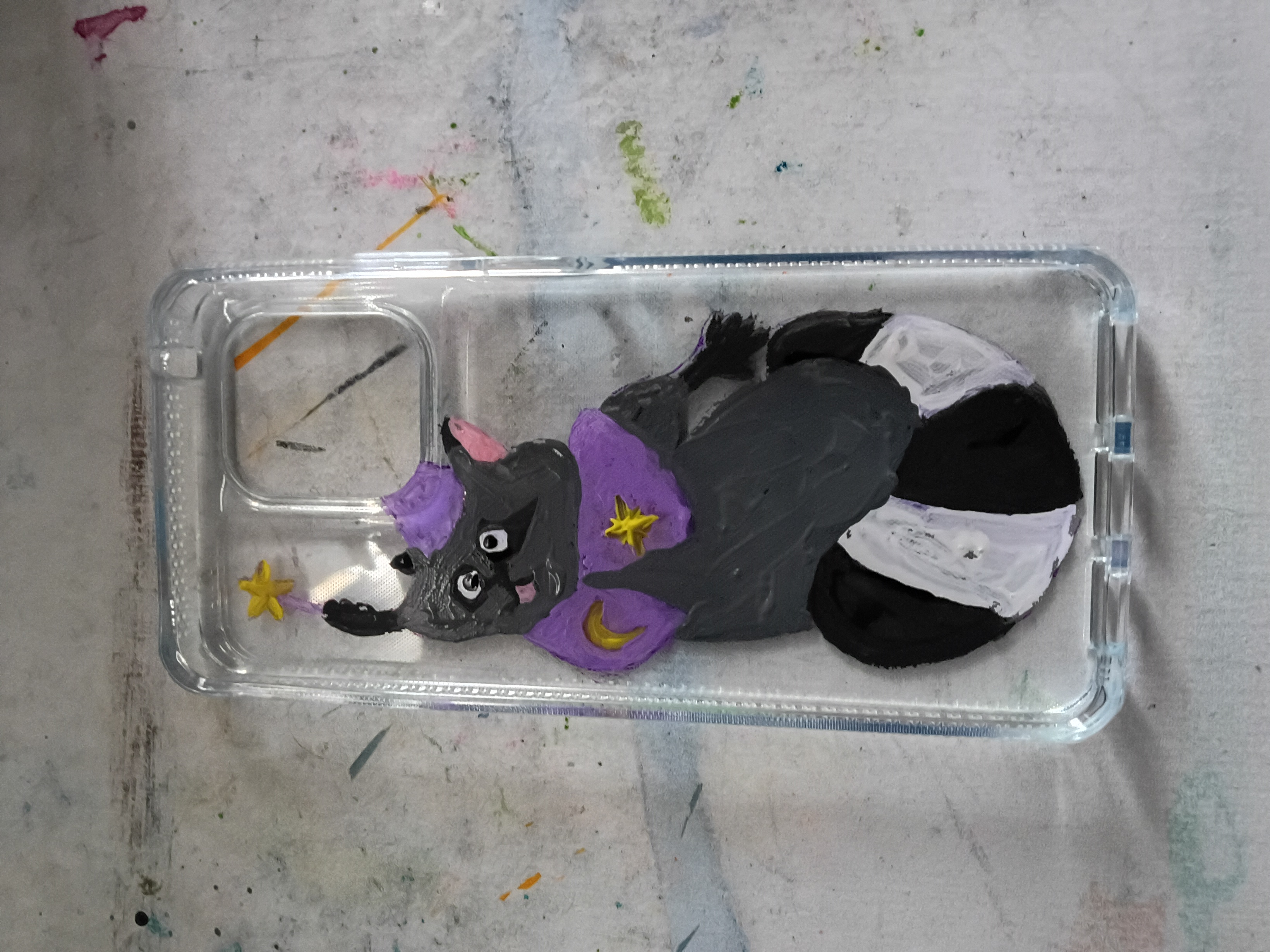 The inside of a clear phone case showing a painted cartoon racoon wearing a wizard cape