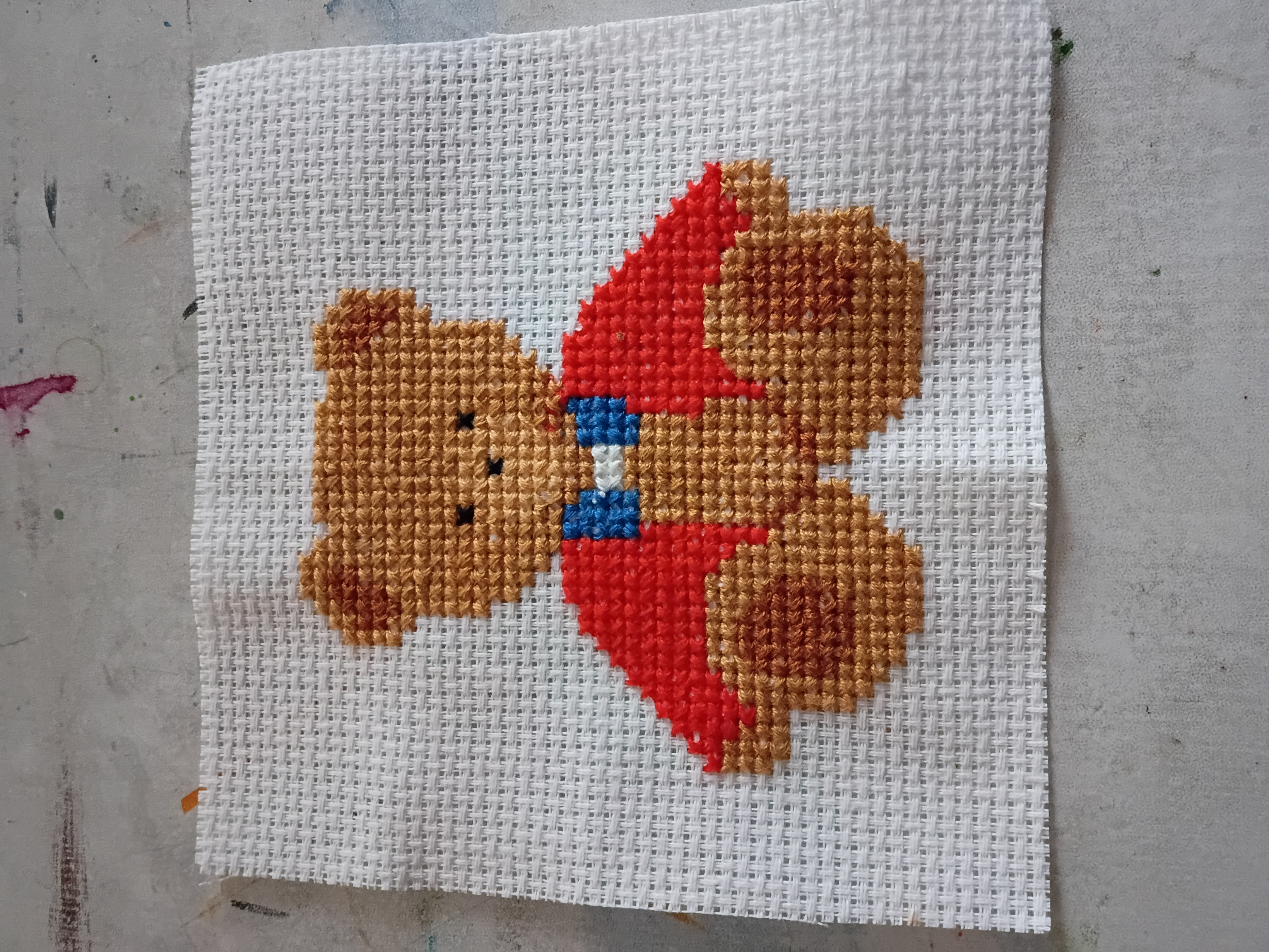 A cross stitch pattern with a bear wearing a red shirt