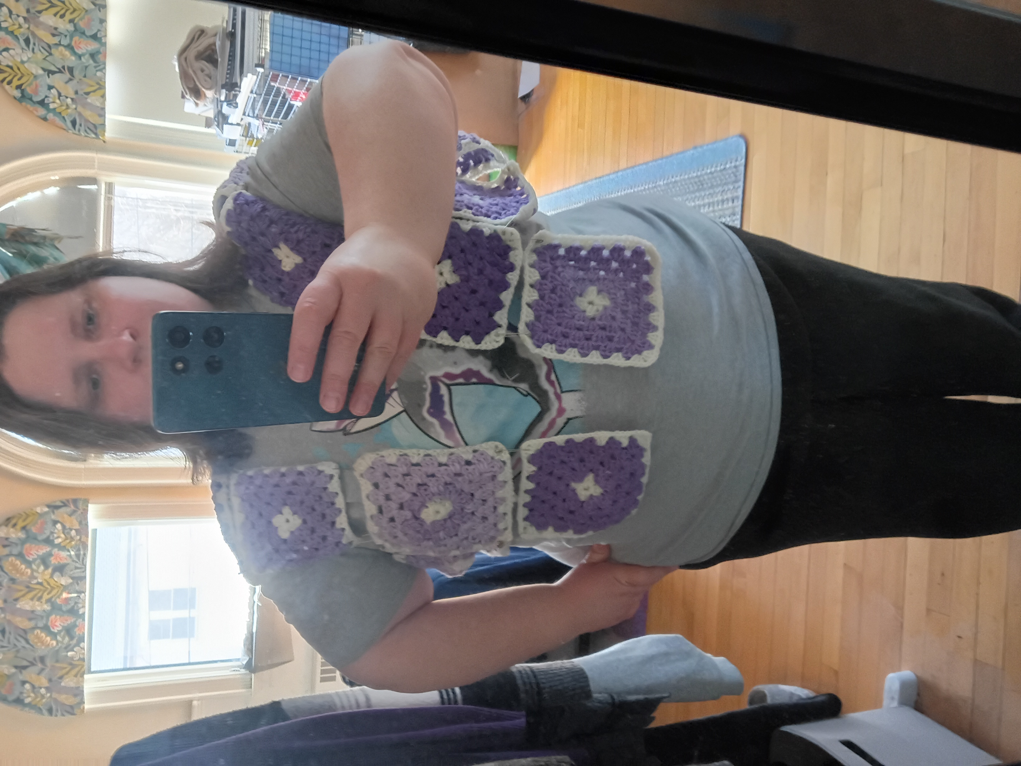 a woman stands in front of a mirror with a few granny squares hanging around her shoulders