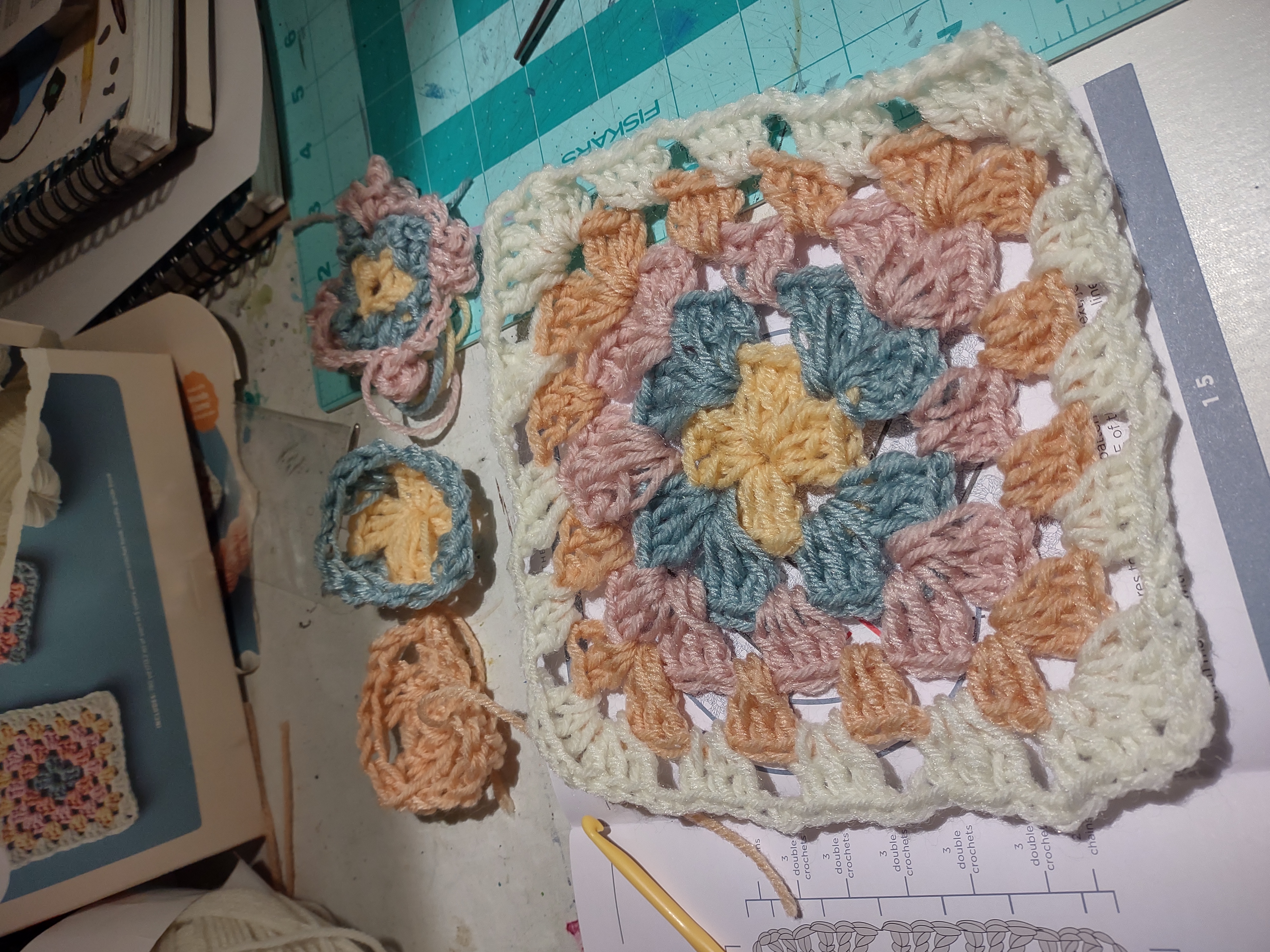 A collection of colorful yarn some are shaped like squares or circles, the one at the front is a granny square