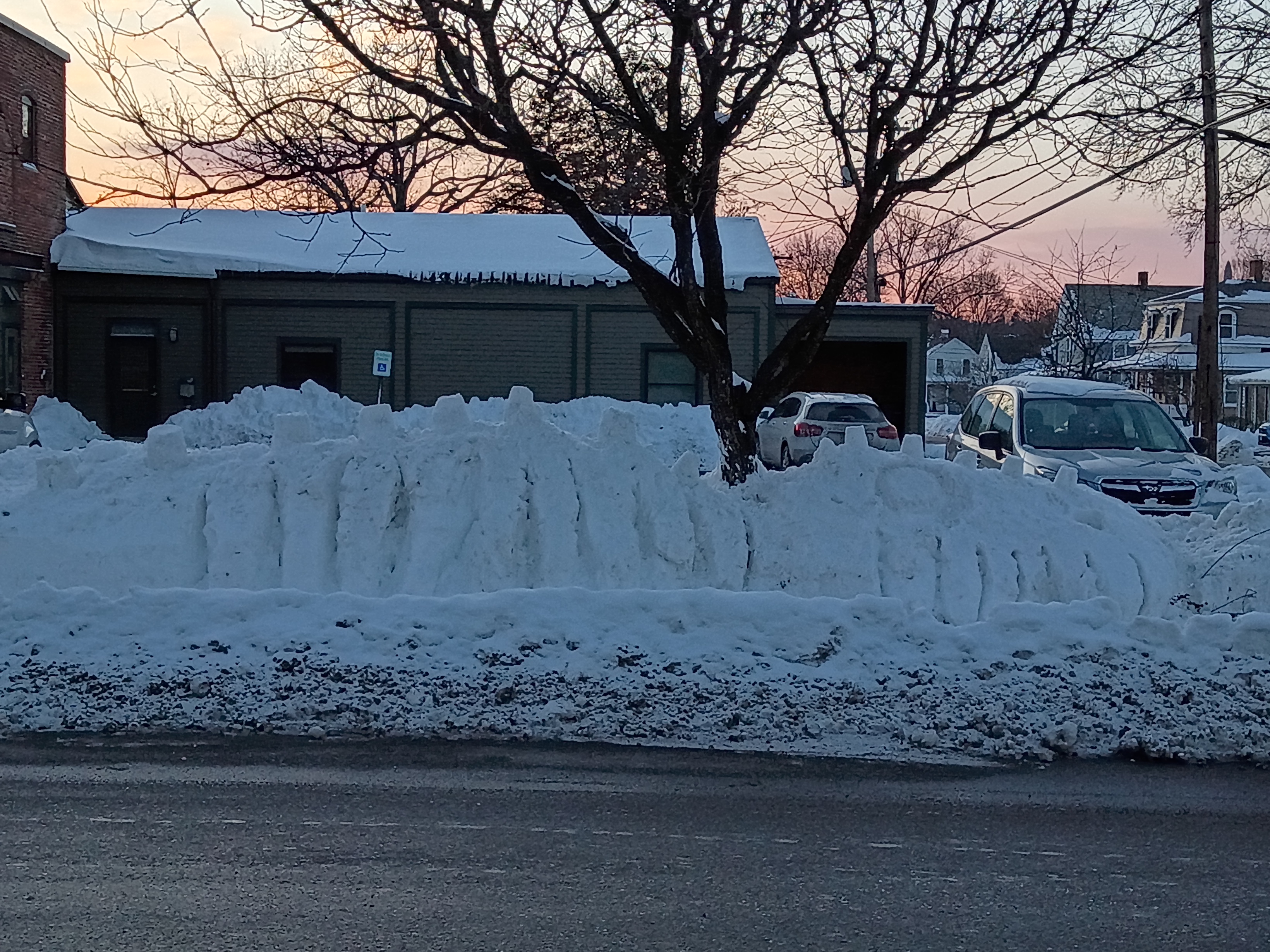 A snow drift in front of a parking lot where the snow has been carved to look like a skeletal creature